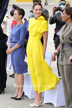 two women in yellow dresses standing next to each other at an air port event with people taking pictures