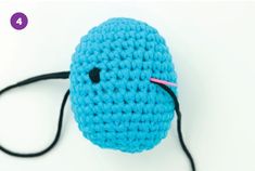 a crocheted blue ball with a black cord on it and a pink stick sticking out of the end