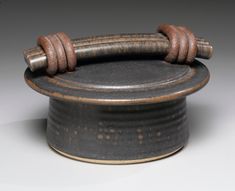 an old black and brown pot with two wooden handles on it's rim, sitting on a white surface