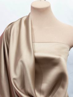 a mannequin wearing a beige dress with one shoulder draped over it