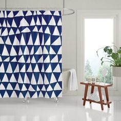 a bathroom with a blue and white shower curtain in front of a window next to a wooden stool