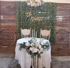 the table is set with white flowers and greenery for an elegant wedding reception in front of a wooden wall