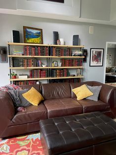 a brown leather couch sitting in front of a book shelf filled with lots of books