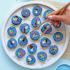 someone is holding chopsticks over some sushi on a white plate with blue water