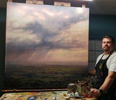 a man standing in front of a painting on a easel next to a table