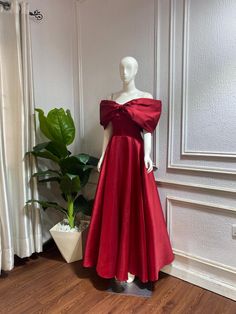 a mannequin dressed in a red dress next to a potted plant