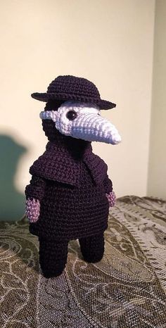 a crocheted bird wearing a hat and coat on top of a bed next to a wall