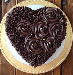 a heart shaped cake with chocolate frosting and flowers on the top is sitting on a plate