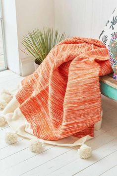 an orange blanket sitting on top of a wooden bench next to a potted plant