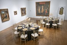 a room filled with tables and chairs covered in black table cloths next to paintings on the wall