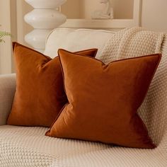 two brown pillows sitting on top of a white couch next to a vase with flowers