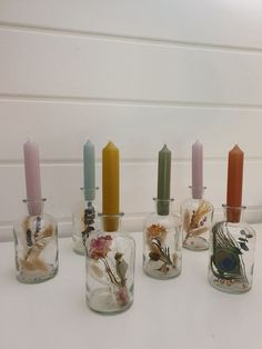 five glass vases with candles in them on a white counter top next to a wall