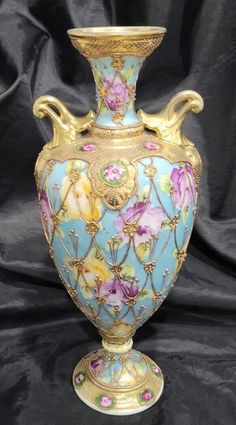 a blue vase with gold trimmings and flowers on the bottom is sitting on a black background