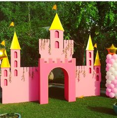 a pink and yellow castle with balloons in the grass next to it on a sunny day