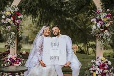 a bride and groom pose for a photo under an arch decorated with floral arrangements at their wedding