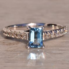 an engagement ring with a blue topazte surrounded by white diamonds on a wooden surface