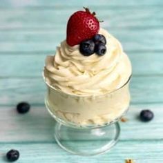 a cupcake with whipped cream and fresh berries on top is sitting in a glass dish