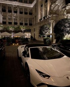 a white sports car parked in front of a hotel at night with its lights on