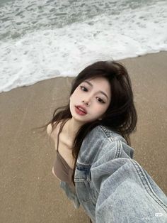 a woman laying on top of a sandy beach next to the ocean with waves coming in