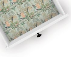 a white shelf with a wallpaper pattern on it and a black knob in the middle