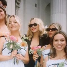 a group of women standing next to each other in front of a building holding flowers