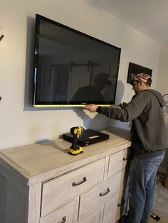 a man standing in front of a flat screen tv holding a yellow tool and measuring it