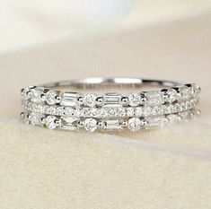 a wedding ring with three rows of diamonds on it's side, sitting on top of a white cloth