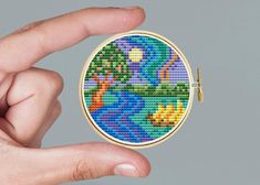 a hand holding a small cross - stitched brooch in it's palm