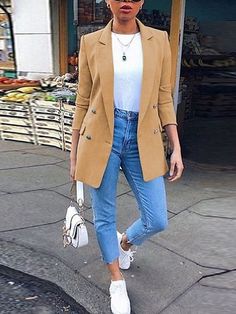 a woman walking down the street wearing sunglasses and a tan blazer with blue jeans