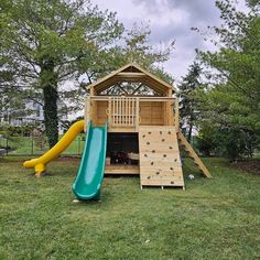 a wooden playset with a slide and climbing wall in the back yard, surrounded by trees