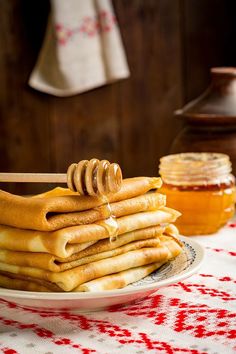 a stack of pancakes on a plate with honey in the background