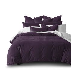 a bed with purple comforter and pillows on top of it in front of a white wall