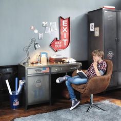 a young boy sitting in a chair reading a book at a desk with lockers on the wall