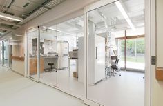 an empty office with glass walls and white flooring is seen from the hallway to the kitchen