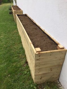 a wooden planter filled with dirt next to a white wall and green grass on the ground