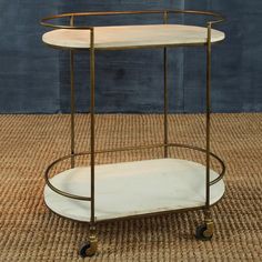 a white and gold serving cart with wheels on carpeted floor next to blue wall