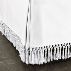 a bed with white sheets and fringes on the bottom edge, in black and white