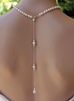 the back of a woman's neck wearing a white necklace with pearls on it