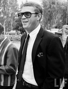 black and white photograph of two men in suits talking to each other while one man is wearing sunglasses