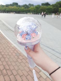 a person holding up a clear plastic object with flowers on it's side and people walking in the background