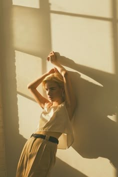 a woman leaning against a wall with her hands behind her head