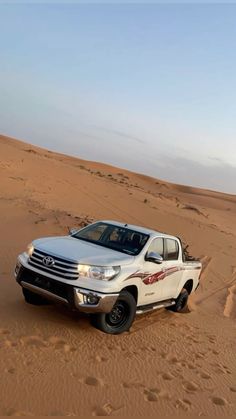 a white truck is driving through the sand dunes in the middle of the desert,