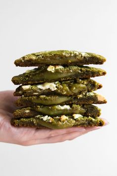 a hand holding a stack of green cookies with cream cheese on top and pickles in the middle