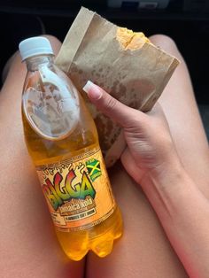 a woman holding a bottle of beer and a paper bag with food in it sitting on the back seat of a car