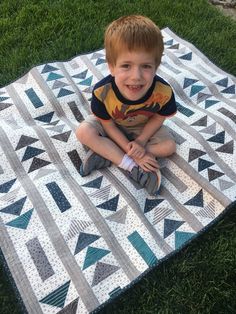 a young boy sitting on top of a quilt in the grass with his feet crossed