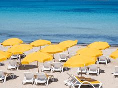 yellow umbrellas and chairs on the beach with blue water in the backgroud