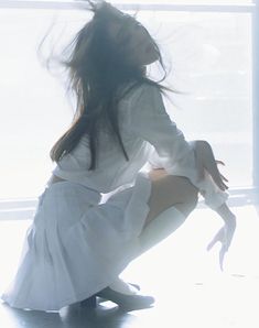 a woman kneeling on the floor with her hair blowing in the wind while wearing a white dress