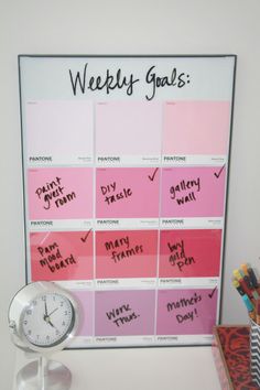 a white clock sitting on top of a desk next to a pink and red calendar