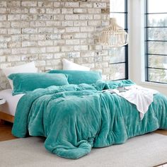 a bedroom with brick wall and turquoise comforter on the bed in front of a window