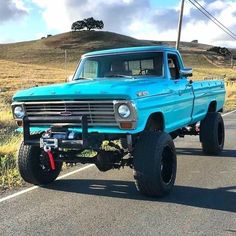 an old blue truck is parked on the side of the road in front of a hill